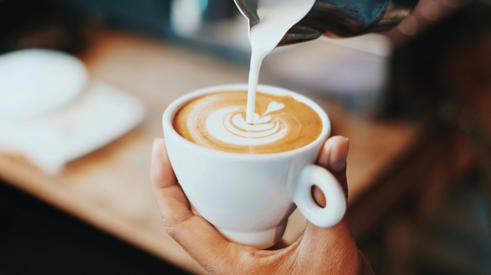 A barista pouring latte art into a white cup